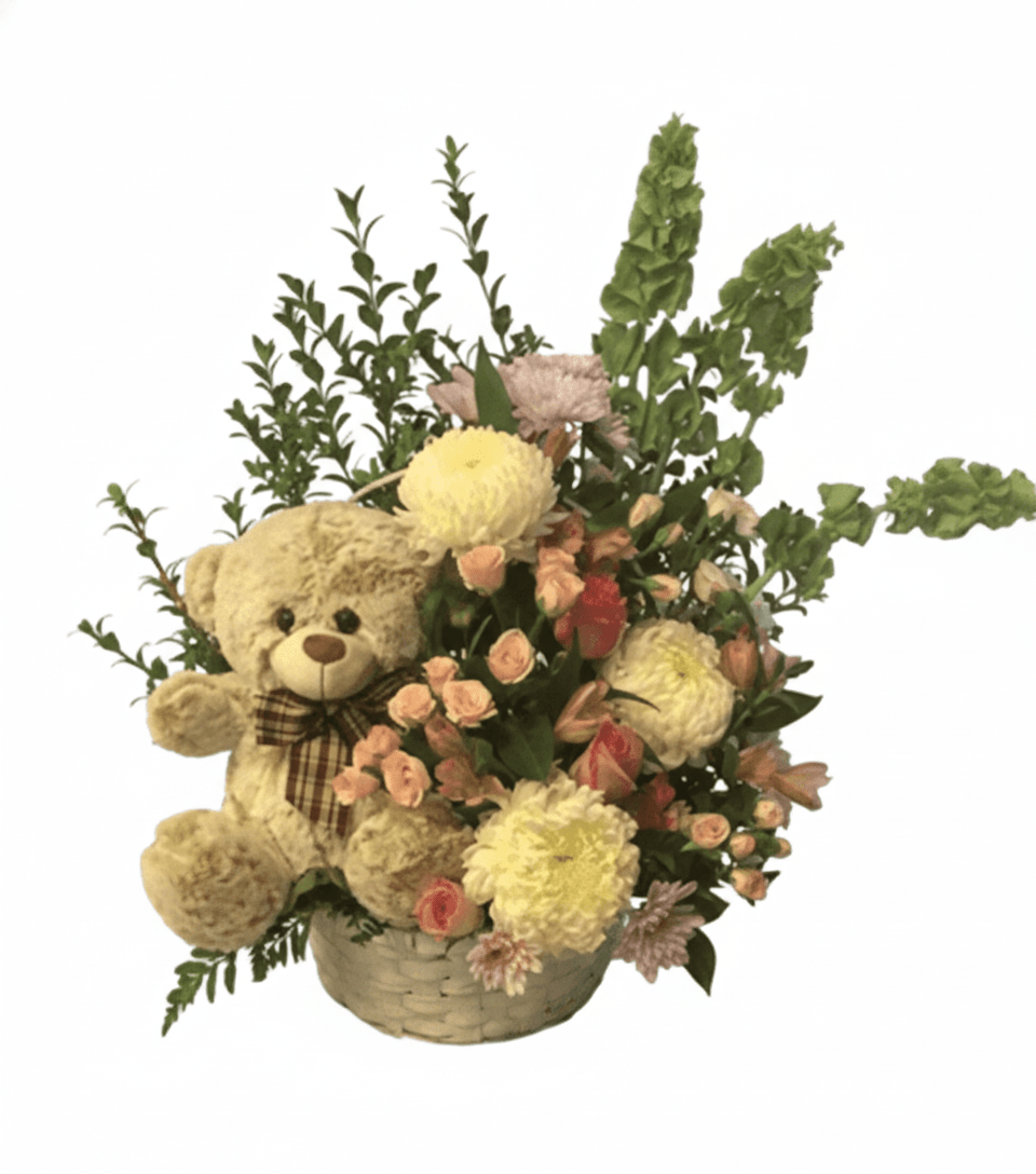 A cheerful floral arrangement featuring a small brown teddy bear tucked amongst bright yellow and orange roses, white daisies, and green accent foliage in a decorative container.