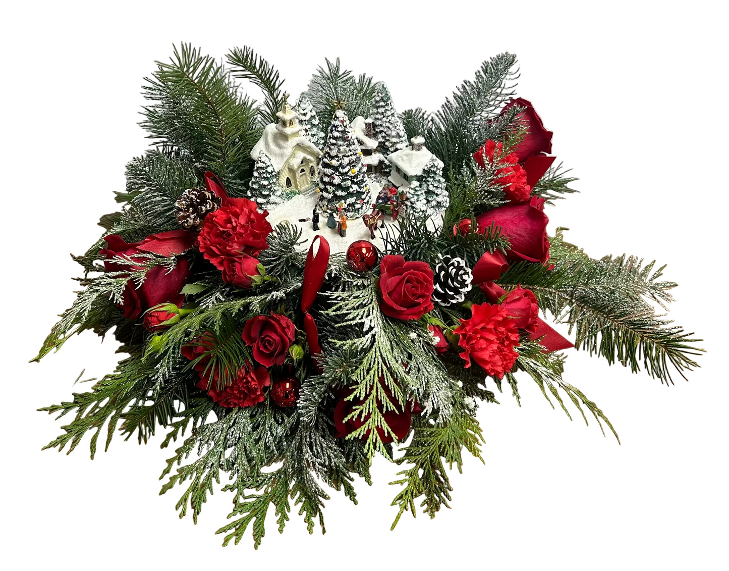 Decorative Christmas arrangement with red flowers, greenery, and snow-dusted pinecones on a wooden floor.
