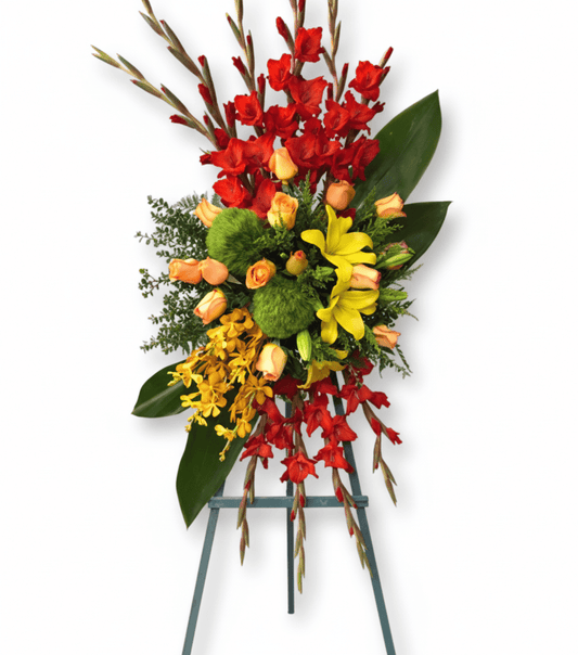 A standing floral spray called Flower of Soul, featuring vibrant red gladiolus, orange roses, yellow lilies, golden orchids, and lush greenery, arranged on a display easel.