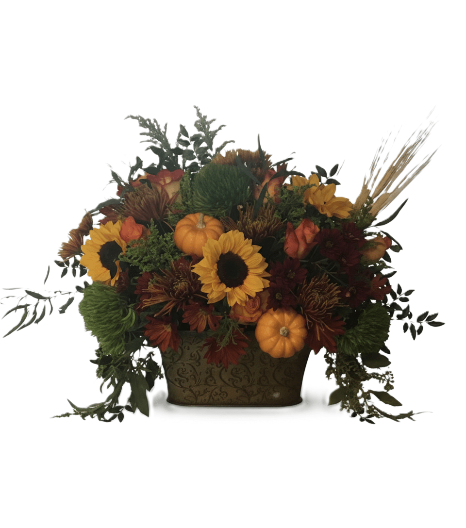 A large, rustic fall floral arrangement in a decorative bronze container, featuring sunflowers, orange and yellow roses, burgundy and green cushion mums, decorative pumpkins, wheat stalks, and various green foliage.