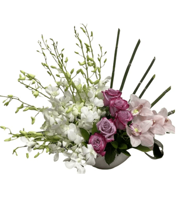 A low, asymmetrical floral arrangement in a white bowl, with white Dendrobium orchids on the left, a cluster of light purple roses and light pink Cymbidium orchids in the center, and tall, straight green stems on the right, against a pure white background.