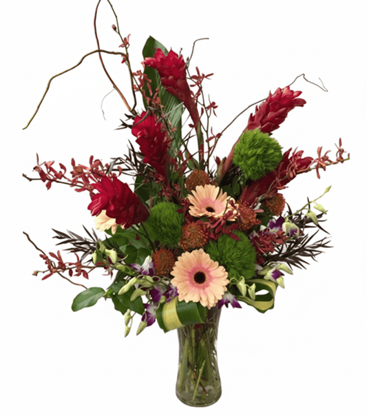 A vibrant, exotic floral arrangement in a clear glass vase against a solid white background. The bouquet features striking red ginger flowers, delicate peach-pink gerbera daisies, fluffy green textural elements, small reddish-brown orchids, and dark green foliage with some slender dried branches reaching upwards.