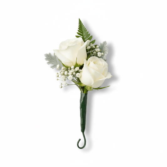 A white rose boutonnière with two fully bloomed white roses, delicate baby's breath, green fern, and dusty miller foliage, all wrapped with a dark green stem, against a pure white background.