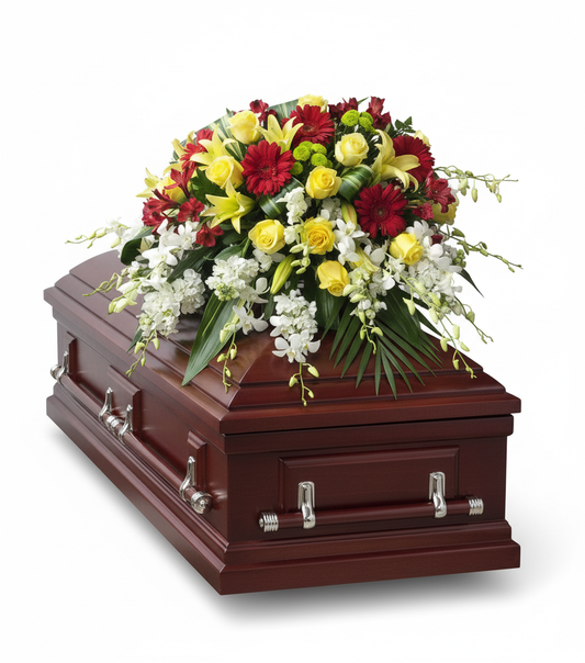 A large funeral spray featuring a variety of purple, pink, and white flowers, including hydrangeas and roses, placed on a closed wooden coffin.