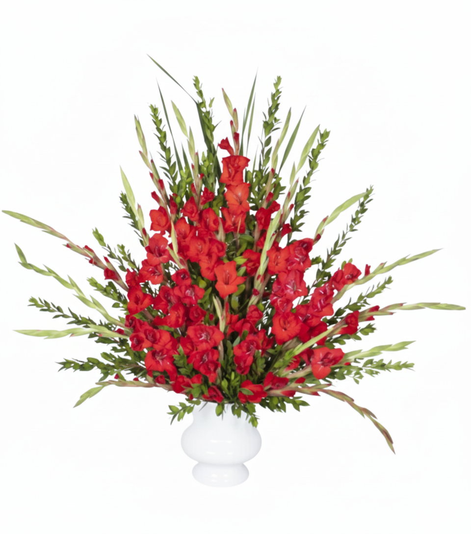 A tall, dramatic floral arrangement in a white pedestal vase, featuring numerous spikes of vibrant red gladiolus flowers and their vertical green leaves, against a pure white background.