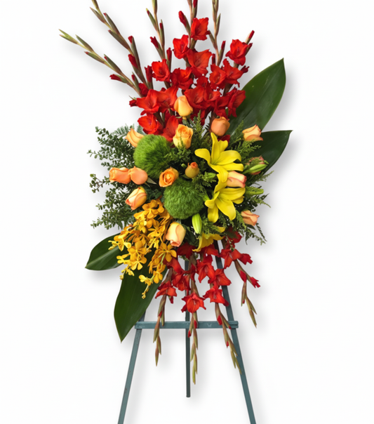 A standing floral spray called Flower of Soul, featuring vibrant red gladiolus, orange roses, yellow lilies, golden orchids, and lush greenery, arranged on a display easel.