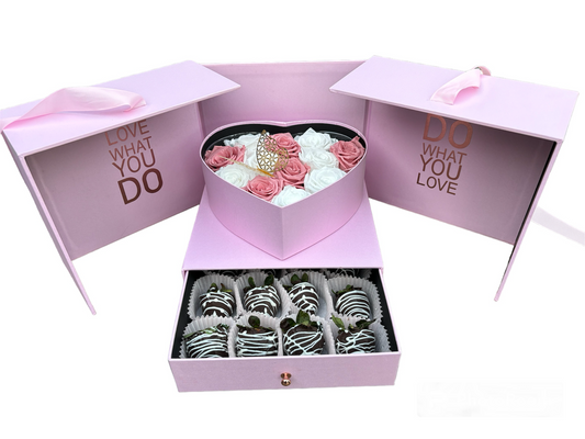 Pink gift box with heart-shaped lid containing flowers and a smaller box with chocolate-covered treats.