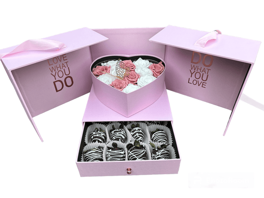 Pink gift box with heart-shaped lid containing flowers and a smaller box with chocolate-covered treats.