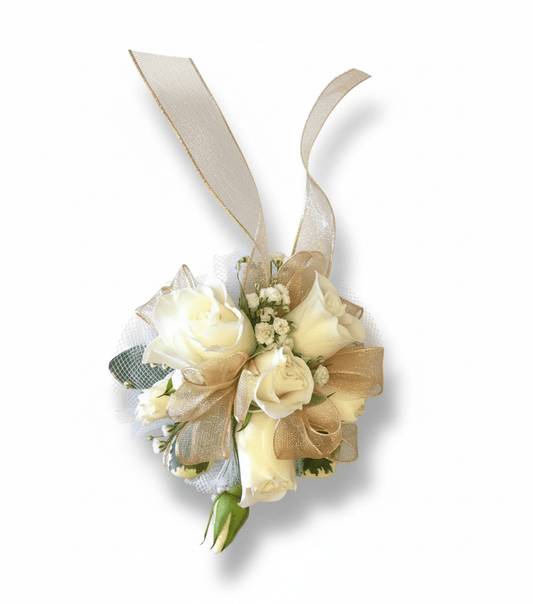 A elegant wrist corsage featuring creamy white spray roses, delicate baby's breath, and a touch of greenery, adorned with shimmering gold sheer ribbon loops and longer trailing gold ribbons, all set against a pure white background.