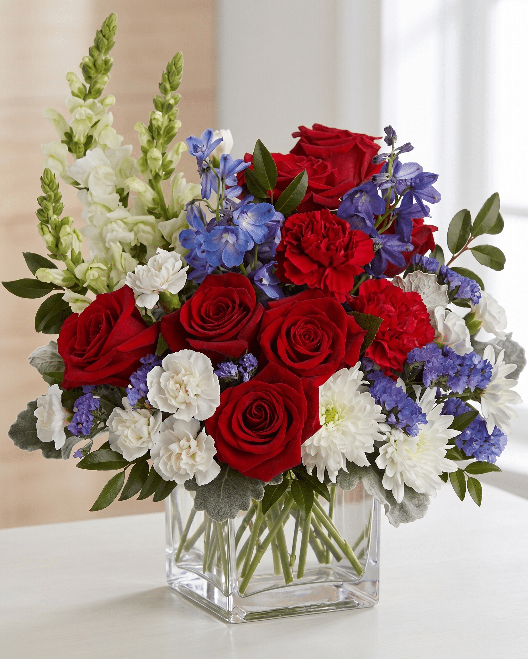 Bouquet of red roses, white flowers, and blue delphinium in a clear glass vase.