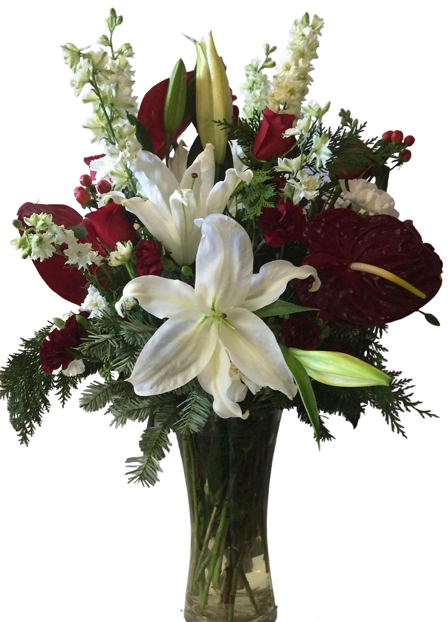 Bouquet of flowers with white lilies, red roses, and greenery in a clear vase on a white background
