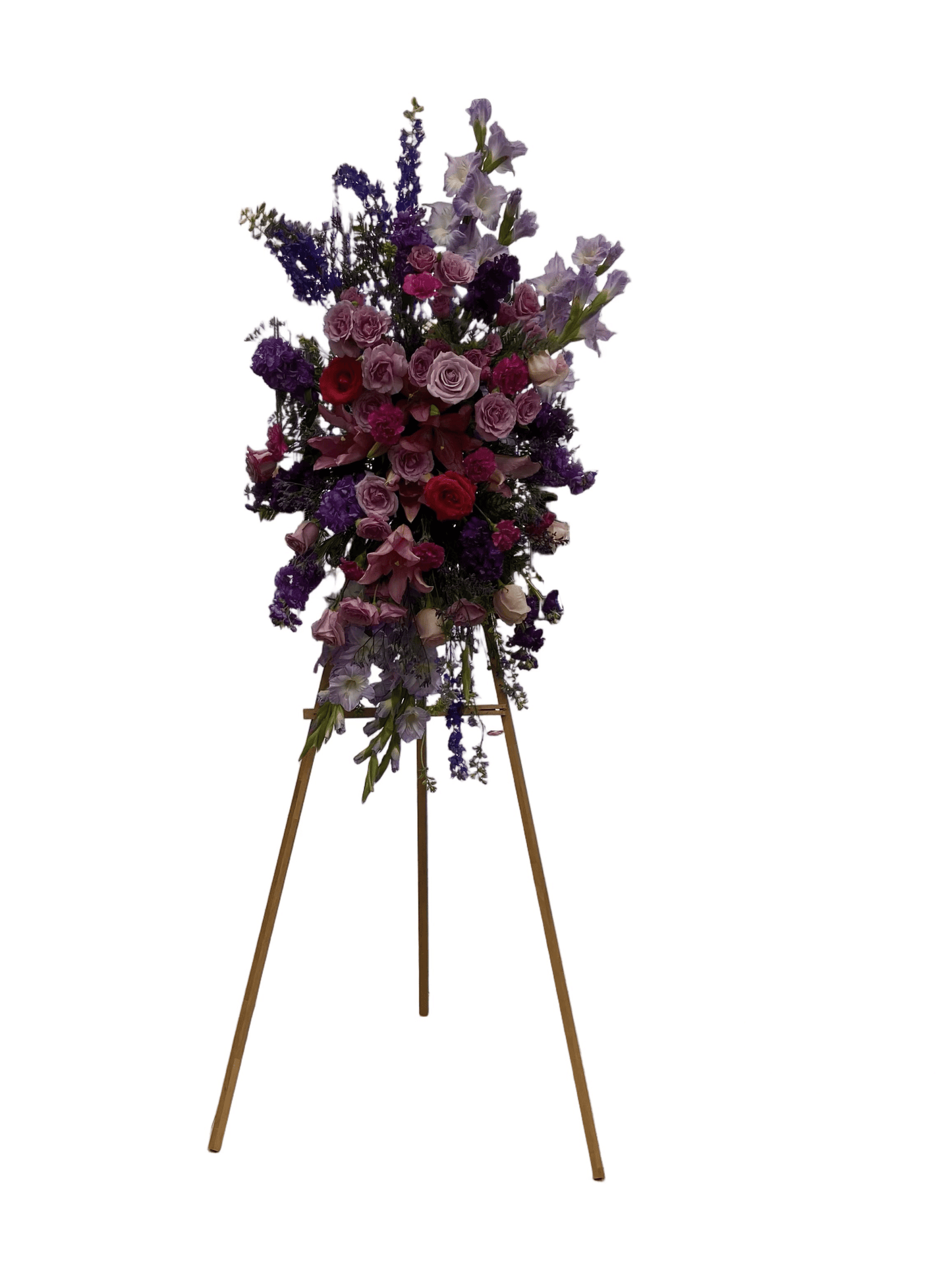 Funeral flower arrangement in shades of purple and pink, presented on a light brown wooden stand, with a clear white background.