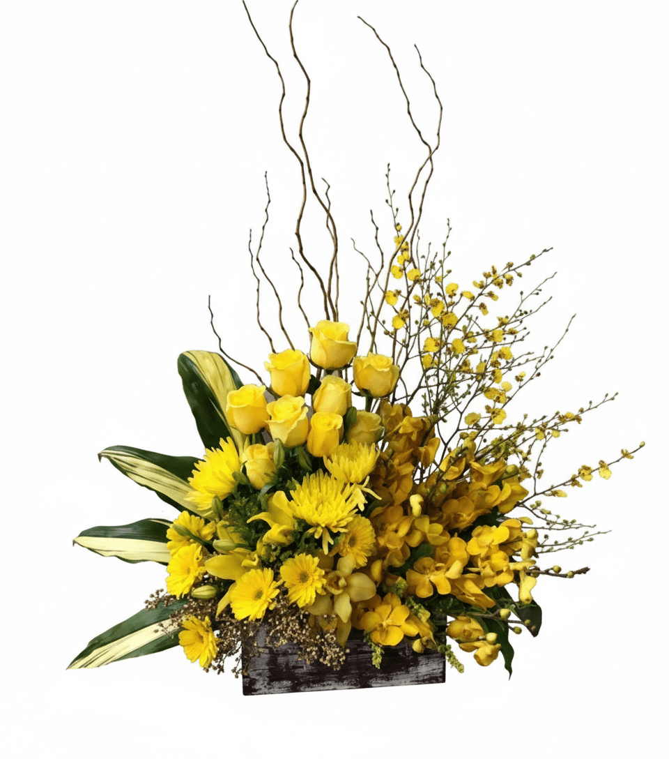 A vibrant, asymmetrical floral arrangement called "Marvelous Basket" in a rustic wooden box, set against a solid white background. The arrangement is dominated by various shades of yellow flowers including roses, chrysanthemums, and delicate spray orchids, complemented by variegated green and white leaves and tall, slender brown branches.