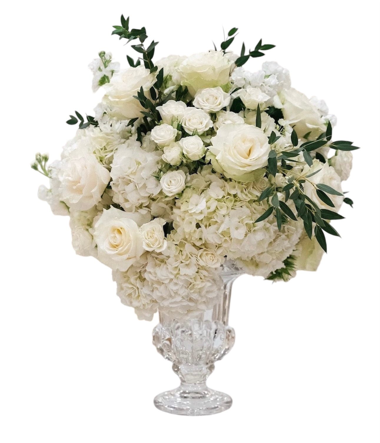 Floral arrangement with white flowers and greenery in a clear glass vase on a white background