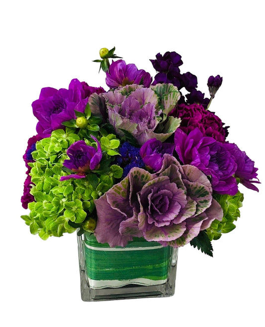 Bouquet of purple and green flowers in a clear vase on a white background