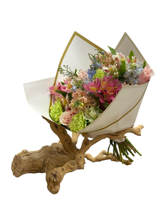 Bouquet of flowers wrapped in white paper with gold edges on a wooden base against a white background