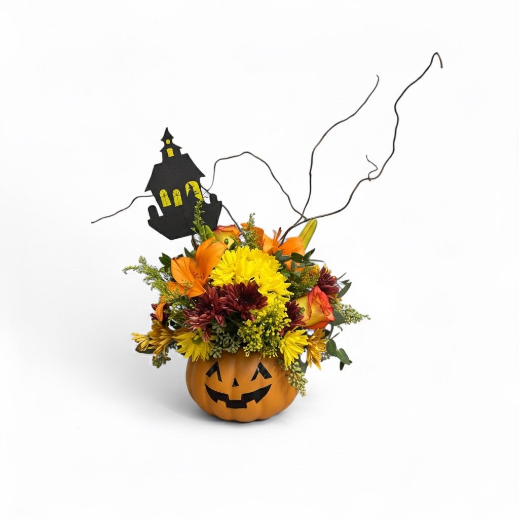 Halloween-themed flower arrangement in a pumpkin with a haunted house decoration on a white background