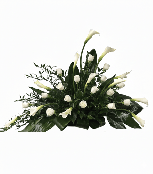 A complete and elegant horizontal floral arrangement named "Purity Of The Soul," featuring numerous white calla lilies and white roses interspersed with rich green foliage, including broad leaves and delicate leafy branches, all set against a solid white background.