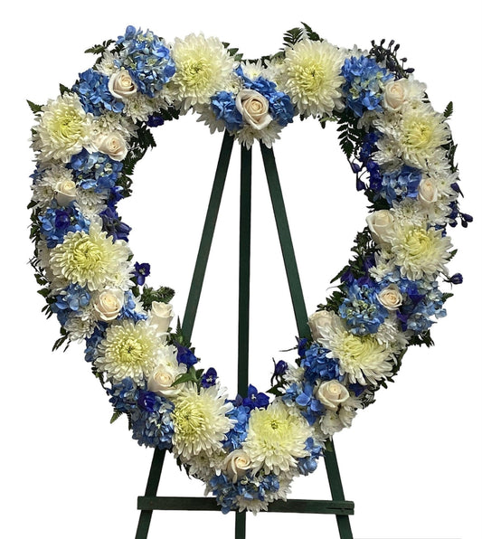 Floral wreath with blue and white flowers on a stand against a white background