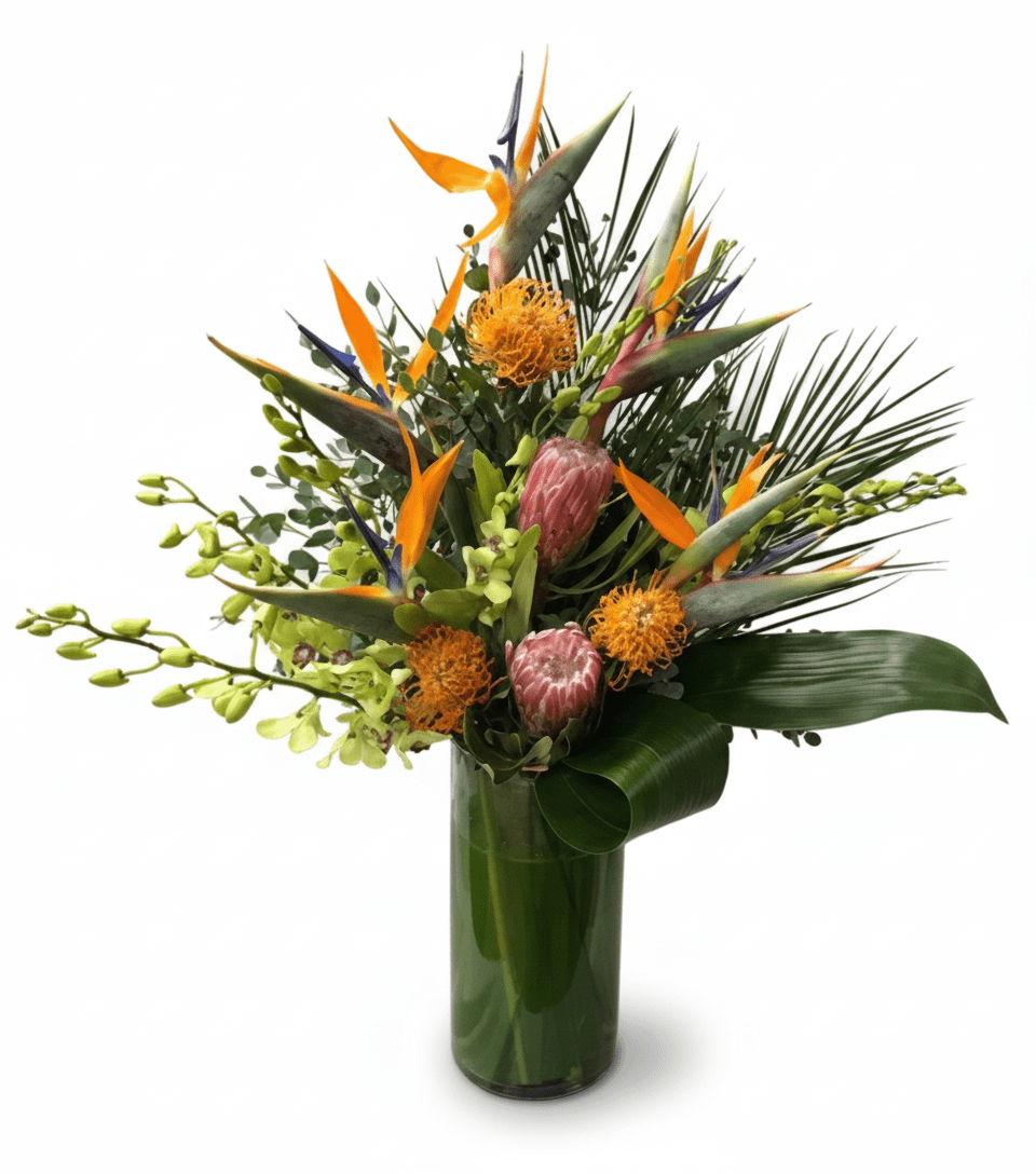 A striking tropical floral arrangement in a tall green glass vase, featuring bright orange birds of paradise, orange pincushion protea, pink protea, green orchid sprays, and various palm and exotic green leaves.