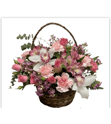 A large floral basket arrangement with a handle, filled with a variety of pink and white flowers including spray roses, carnations, orchids, and alstroemeria, complemented by green foliage, against a pure white background.