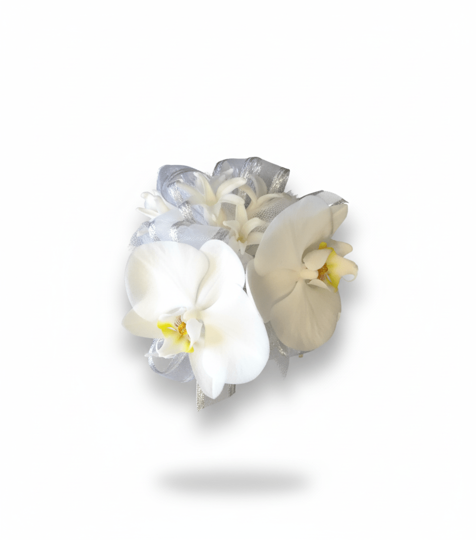 A sophisticated wrist corsage featuring two elegant white Phalaenopsis orchid blooms with yellow centers, accented by delicate white filler flowers and shimmering silver and white sheer ribbons, all against a pure white background.